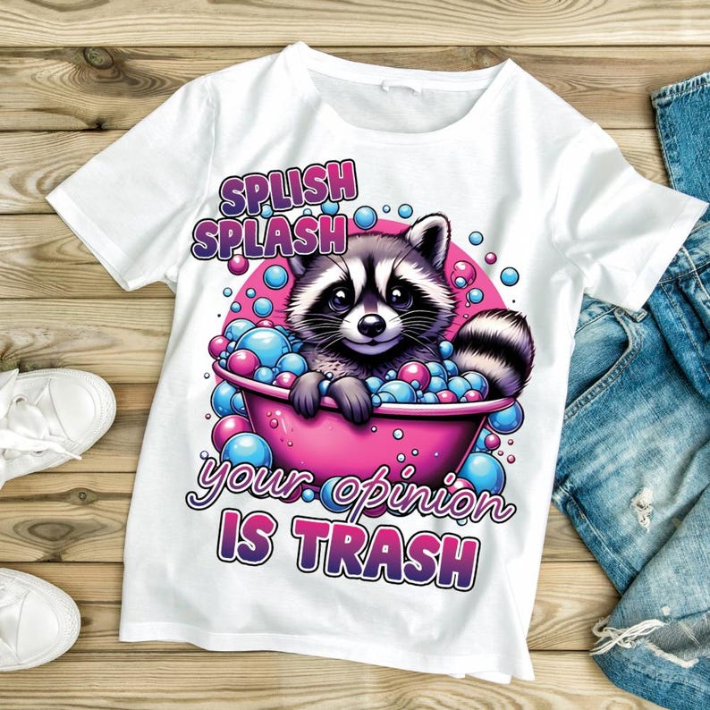 May include: White t-shirt featuring a raccoon in a pink bathtub filled with blue and pink bubbles. The raccoon has a black and white face and a striped tail. Text on the shirt reads "Splish Splash your opinion IS TRASH."