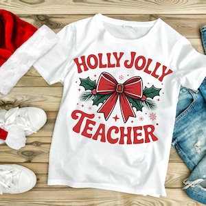 May include: White t-shirt with the text "HOLLY JOLLY TEACHER" in red, featuring a red bow, holly, and snowflakes. The shirt is on a wooden surface with a red Santa hat and white shoes.