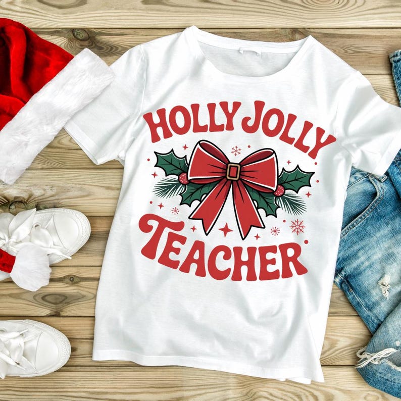 May include: White t-shirt with the text "HOLLY JOLLY TEACHER" in red, featuring a red bow, holly, and snowflakes. The shirt is on a wooden surface with a red Santa hat and white shoes.