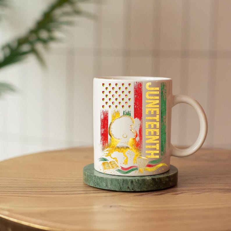 Pu&ograve; includere: Tazza in ceramica bianca con un design Juneteenth. La tazza presenta una bandiera americana stilizzata con strisce rosse e verdi, un'illustrazione dorata e la parola "Juneteenth" in lettere dorate. La tazza &egrave; appoggiata su un sottobicchiere di marmo verde.