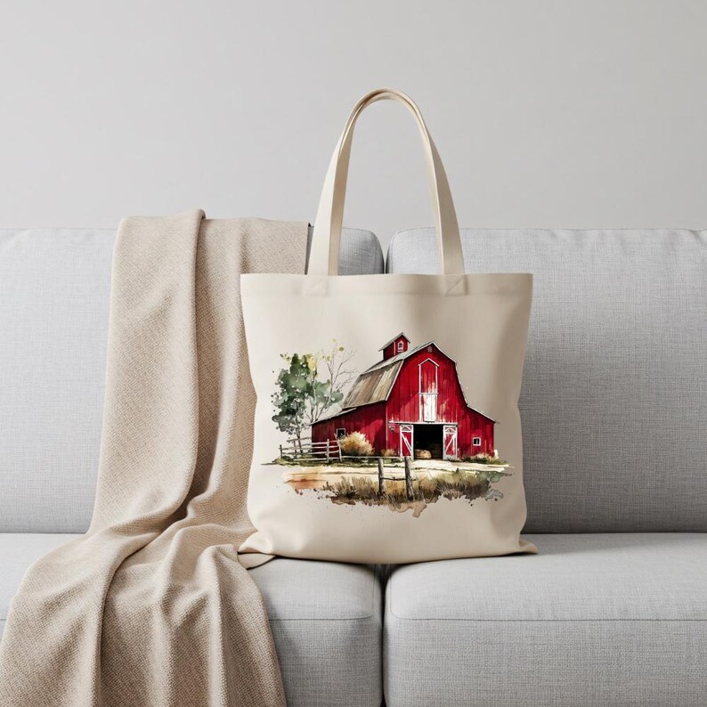 Puede incluir: Un bolso tote color crema con una pintura de acuarela de un granero rojo con puerta y techo blancos. El granero se encuentra frente a &aacute;rboles verdes y una valla de madera, evocando un tema rural y campestre.