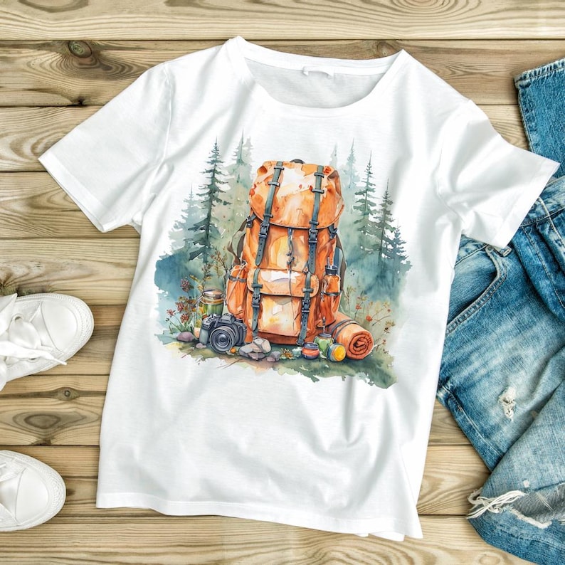 May include: White t-shirt featuring a watercolor illustration of a hiking backpack in shades of orange and brown, with a camera, rolled blanket, and forest backdrop. The design evokes a sense of adventure and outdoor activities.