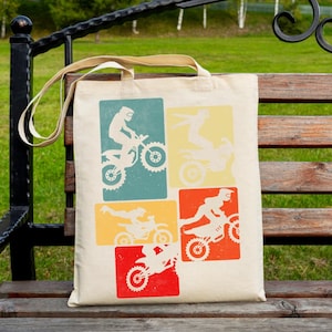 May include: A beige tote bag featuring four retro-style rectangular designs with white silhouettes of motocross riders on motorcycles. The rectangles are in teal, yellow, orange, and red. The bag has beige handles.