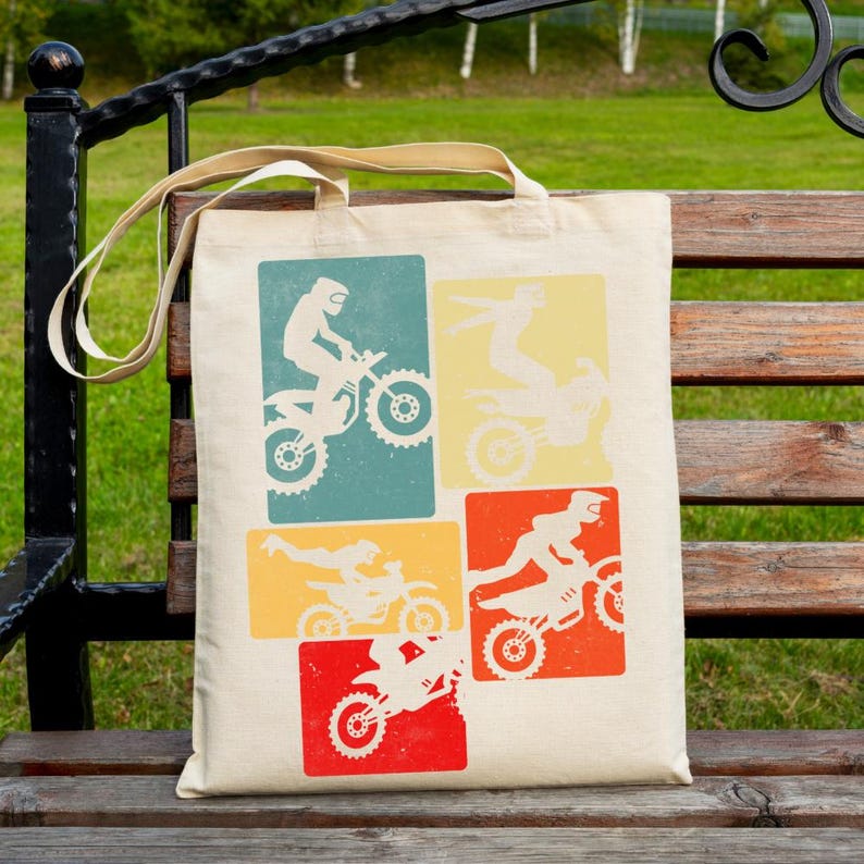 May include: A beige tote bag featuring four retro-style rectangular designs with white silhouettes of motocross riders on motorcycles. The rectangles are in teal, yellow, orange, and red. The bag has beige handles.