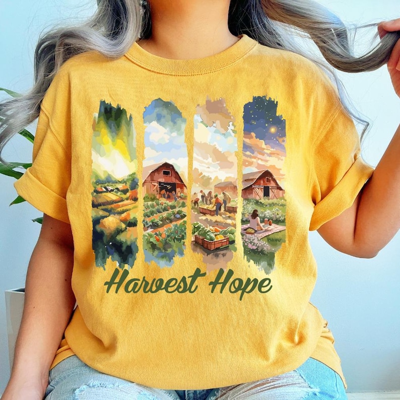 May include: Mustard yellow t-shirt with a watercolor design featuring farm scenes and the text "Harvest Hope" in green. The design includes fields, barns, and people working in a garden.