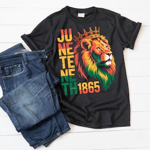 Pu&ograve; includere: T-shirt nero con una grafica di leone colorato con una corona e la scritta "Juneteenth 1865". La maglietta &egrave; abbinata a jeans blu. La grafica del leone presenta colori rosso, giallo e verde.