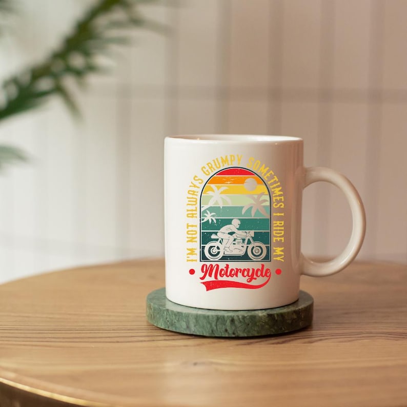 May include: White ceramic mug with a motorcycle design. The mug features the text "I'm not always grumpy, sometimes I ride my motorcycle." The design includes a motorcycle, palm trees, and a sunset.