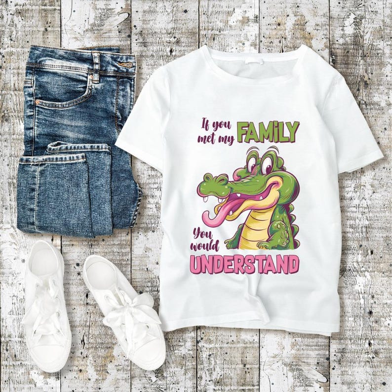 May include: White t-shirt with a cartoon alligator graphic and the text "If you met my FAMILY you would UNDERSTAND". The shirt is paired with blue jeans and white sneakers on a wooden background.