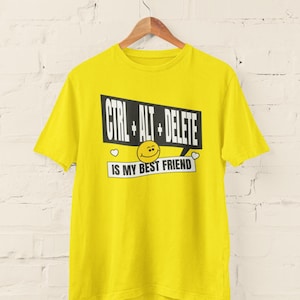 May include: A yellow t-shirt featuring the text "CTRL + ALT + DELETE IS MY BEST FRIEND" in a black and white design. The design includes a smiley face and hearts. The shirt is displayed on a wooden hanger.