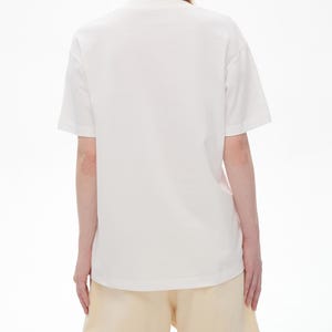 May include: A white t-shirt and light yellow shorts. The t-shirt has short sleeves and a crew neck. The shorts are a light yellow color and have a relaxed fit. The outfit is simple and casual.