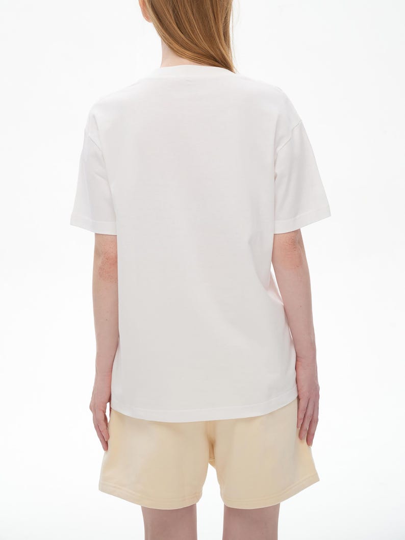 May include: A white t-shirt and light yellow shorts. The t-shirt has short sleeves and a crew neck. The shorts are a light yellow color and have a relaxed fit. The outfit is simple and casual.