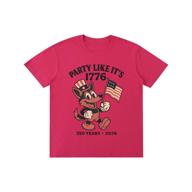 May include: A bright pink t-shirt featuring a cartoon fox holding an American flag. The fox wears a patriotic hat and the shirt reads "PARTY LIKE IT'S 1776" with "250 YEARS &bull; 2026" below.
