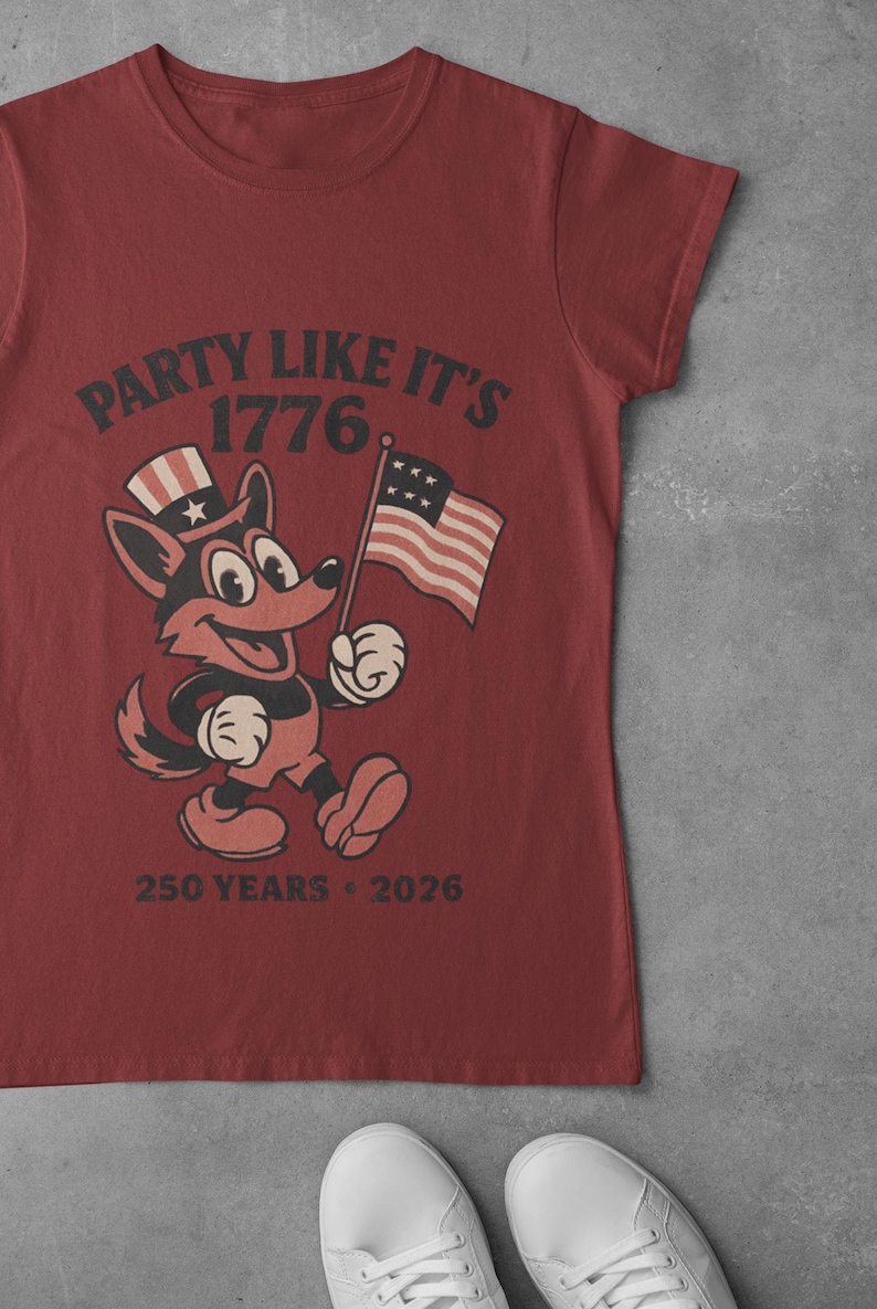 May include: Red t-shirt featuring a cartoon fox wearing a patriotic hat and holding an American flag. The shirt has the text "PARTY LIKE IT'S 1776" and "250 YEARS - 2026".