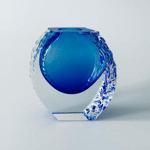 May include: A blue glass vase with a clear glass outer layer. The outer layer has a textured design.