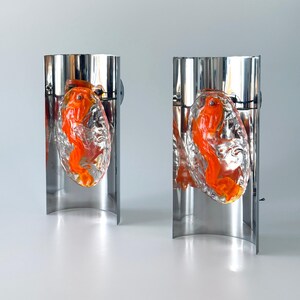 May include: A pair of silver wall sconces with orange glass fish inside. The fish are encased in clear glass and appear to be swimming.