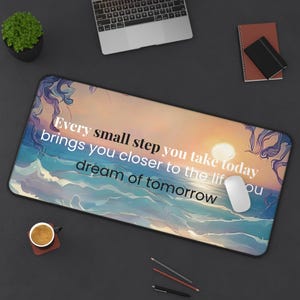 Peut inclure: Un tapis de bureau rectangulaire illustrant un coucher de soleil sur l'océan avec des tons violets, bleus et orange. Le texte indique : Every small step you take today brings you closer to the life you dream of tomorrow. Une souris blanche est posée.