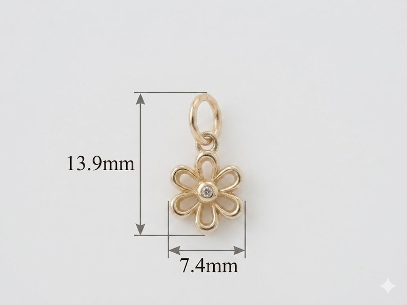 May include: A gold-colored flower charm with a small diamond in the center. The charm is 0.55 inches long and 0.29 inches wide. It has a loop at the top for attaching to a necklace or bracelet. The charm is set against a white background.