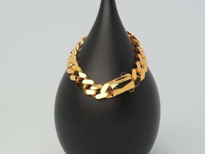 May include: A gold chain bracelet with a curb link design. The bracelet is displayed on a black stand.