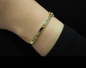 以下が含まれることがあります： 小さな黒い石のアクセントが付いた金のバングルブレスレット。ブレスレットは開いており、ハンマード加工が施されています。