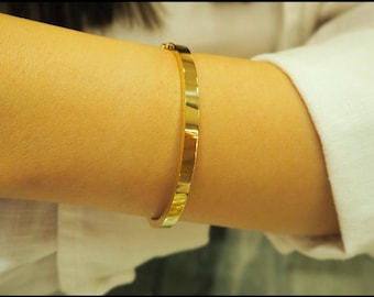 May include: A gold bangle bracelet with a textured surface.