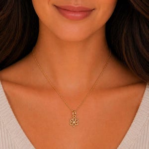 May include: A gold-colored necklace with a flower pendant. The pendant is a delicate openwork design with six petals and a small gem in the center. The necklace is worn around the neck.