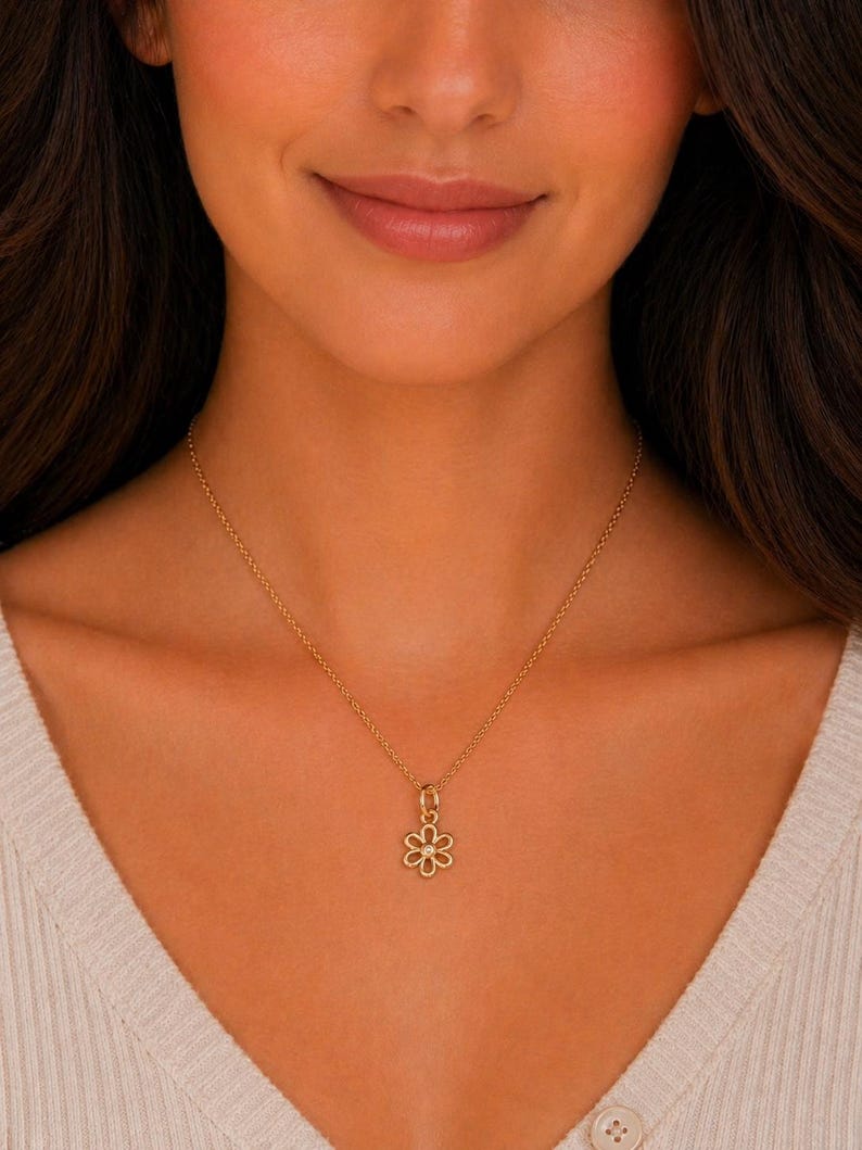 May include: A gold-colored necklace with a flower pendant. The pendant is a delicate openwork design with six petals and a small gem in the center. The necklace is worn around the neck.