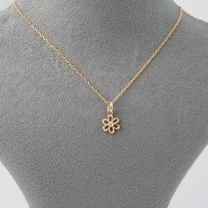 May include: A delicate gold necklace featuring a daisy pendant with a small, clear gemstone at its center. The chain and pendant are a warm gold color, creating a simple yet elegant piece of jewelry.