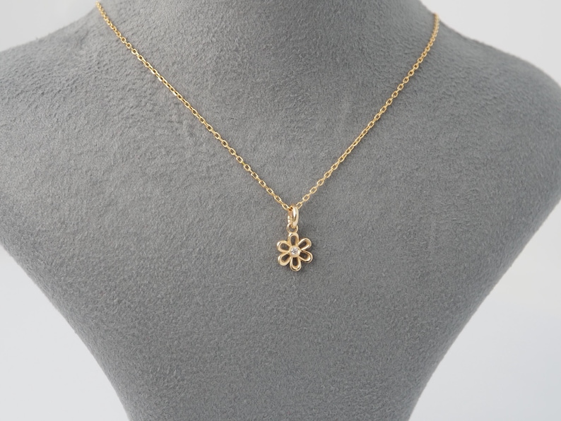 May include: A delicate gold necklace featuring a daisy pendant with a small, clear gemstone at its center. The chain and pendant are a warm gold color, creating a simple yet elegant piece of jewelry.