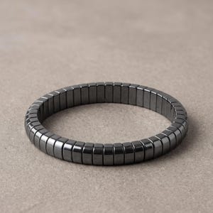 May include: A circular bracelet composed of numerous small, rectangular, dark grey metallic beads with a smooth, polished finish. The beads are arranged in a continuous, uniform row, creating a sleek, segmented appearance for this wrist accessory.