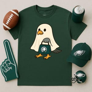 Può includere: T-shirt verde scuro con un uccello dei cartoni animati in costume da fantasma che tiene in mano una borsa verde acqua con il logo della squadra. Include un pallone da football, un dito di schiuma, un cappello, un casco e una lattina.