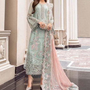 May include: A light blue and pink embroidered dress with a long, flowing skirt and a matching dupatta. The dress has intricate floral and geometric patterns and is adorned with delicate lace.