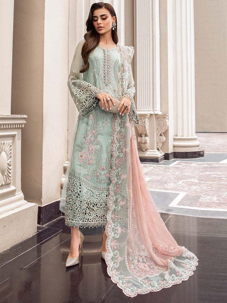May include: A light blue and pink embroidered dress with a long, flowing skirt and a matching dupatta. The dress has intricate floral and geometric patterns and is adorned with delicate lace.