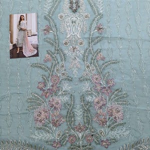 May include: A light blue fabric with a delicate floral pattern embroidered in white and pink. The fabric has a sheer, almost translucent quality.