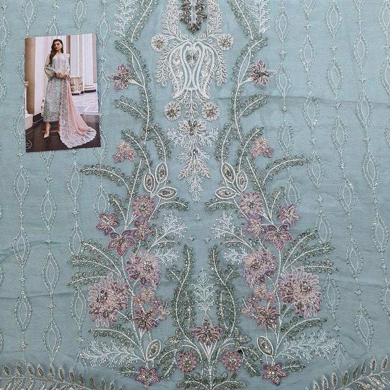 May include: A light blue fabric with a delicate floral pattern embroidered in white and pink. The fabric has a sheer, almost translucent quality.