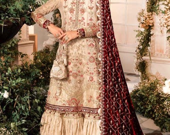 Op de afbeelding: Een crèmekleurige geborduurde jurk met een bordeauxrode fluwelen dupatta. De jurk heeft een gerimpelde zoom en ingewikkelde bloemenborduursels. De dupatta heeft een parelrand en een delicaat bloemenpatroon.