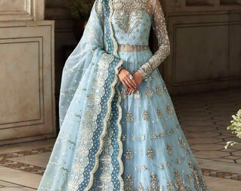 Puede incluir: Un vestido de fiesta azul claro con intrincados bordados y adornos plateados. El vestido presenta mangas largas, un corpiño transparente y una falda fluida. Un chal a juego con un ribete detallado completa el elegante conjunto.