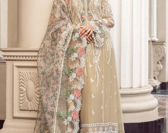 Könnte beinhalten: Ein beigefarbenes Chiffonkleid mit aufwendigen Blumenstickereien und Spitzendetails. Das Kleid hat lange Ärmel und einen runden Ausschnitt. Das Model trägt ein passendes Dupatta mit Blumenmuster und Spitzenbesatz.