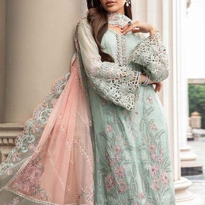 May include: A light blue and pink embroidered dress with intricate lace detailing. The dress has a long, flowing silhouette and a high neckline. The fabric is sheer and delicate, and the dress is adorned with sparkling embellishments.