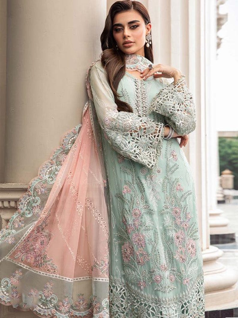May include: A light blue and pink embroidered dress with intricate lace detailing. The dress has a long, flowing silhouette and a high neckline. The fabric is sheer and delicate, and the dress is adorned with sparkling embellishments.