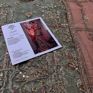 Peut inclure: Gros plan sur un tissu brod&eacute; vert et rose avec des paillettes et des perles. Le tissu est en filet et pr&eacute;sente un motif d&eacute;licat et complexe. Le tissu est pr&eacute;sent&eacute; avec une &eacute;tiquette qui indique "Zariish by Humaira" et "Zamurd".