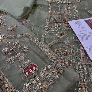 Peut inclure: Un tissu transparent vert clair avec des broderies complexes en argent, or et rouge. La broderie pr&eacute;sente des motifs floraux, des motifs g&eacute;om&eacute;triques et un petit motif de vase. Le tissu est d&eacute;licat et translucide, avec un effet chatoyant.