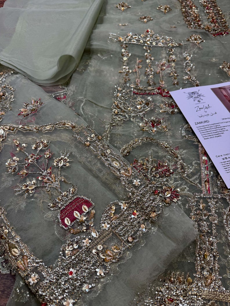 Peut inclure: Un tissu transparent vert clair avec des broderies complexes en argent, or et rouge. La broderie pr&eacute;sente des motifs floraux, des motifs g&eacute;om&eacute;triques et un petit motif de vase. Le tissu est d&eacute;licat et translucide, avec un effet chatoyant.