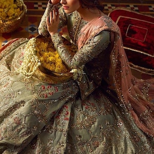 Peut inclure: Une femme portant une robe brod&eacute;e verte et dor&eacute;e avec un dupatta rose. Elle tient un bol de fleurs jaunes et est assise sur un sol &agrave; motifs.