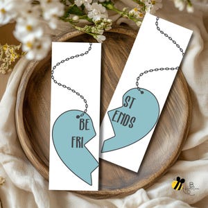 Puede incluir: Dos marcapáginas blancos con un diseño de corazón roto azul claro. Uno dice "BE FRI" y el otro "ST ENDS", formando "Best Friends" cuando se combinan. Cada marcapáginas tiene una cadena plateada.