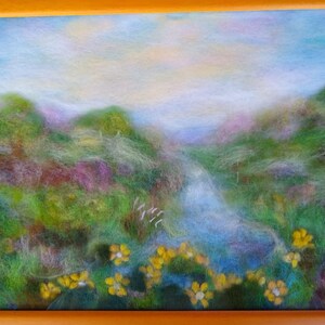 May include: A framed landscape art piece featuring a serene scene. The artwork depicts a valley with a stream, lush green hills, and yellow flowers in the foreground. The sky is a soft blue with hints of yellow.