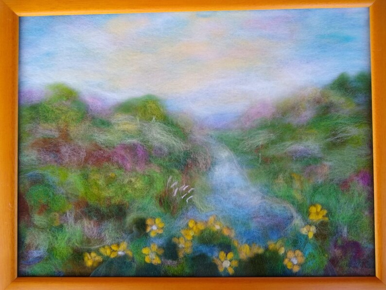 May include: A framed landscape art piece featuring a serene scene. The artwork depicts a valley with a stream, lush green hills, and yellow flowers in the foreground. The sky is a soft blue with hints of yellow.