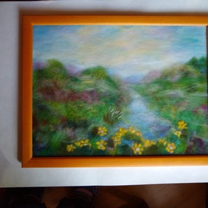 May include: A framed landscape painting featuring a serene river scene. The artwork showcases a vibrant palette of greens, blues, and yellows, with a focus on the natural beauty of the landscape. The frame is a warm orange color.