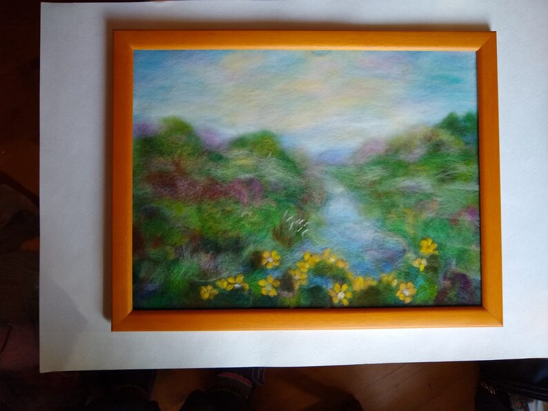 May include: A framed landscape painting featuring a serene river scene. The artwork showcases a vibrant palette of greens, blues, and yellows, with a focus on the natural beauty of the landscape. The frame is a warm orange color.