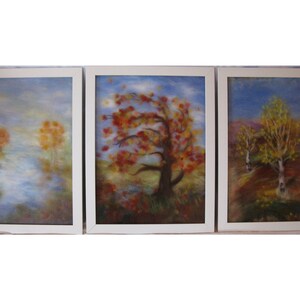 May include: A triptych of framed art pieces depicting autumnal landscapes. Each piece features a white frame and showcases trees with vibrant red, orange, and yellow foliage against a backdrop of blue skies and soft, muted colors. The artwork evokes a sense of tranquility.