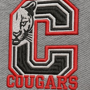 May include: Close-up of grey fabric with an embroidered design. The design features a large letter "C" in black, white, and red, with a cougar head on the left. The word "COUGARS" is embroidered in red below the letter.